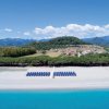 Spiaggia con ombrelloni, mare turchese e colline verdi.