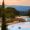 Piscina con ponticello e panorama montano al tramonto.