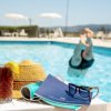 Tavolino a bordo piscina con drink, cappello e occhiali da sole.