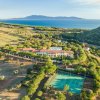 Veduta panoramica di un hotel con campi da tennis, circondato da verde, mare e colline.