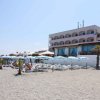Facciata di un hotel fronte mare con ombrelloni e persone sulla spiaggia.