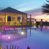 Una piscina illuminata di notte con gazebo bianco accanto e cielo al tramonto.
