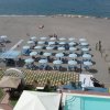 Spiaggia con ombrelloni a righe bianche e blu, lettini e una piscina in primo piano.
