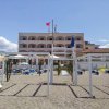 Spiaggia con lettini e una struttura bianca, dietro un edificio a più piani con bandiere in cima.