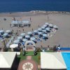 Vista dall'alto di una spiaggia con ombrelloni blu e bianchi, vicino a una piscina e un'area verde.