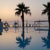 Piscina con riflessi di palme al tramonto, atmosfera serena e luminosa.