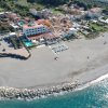 Vista aerea di una spiaggia con un hotel, ombrelloni, e un breve molo di rocce.