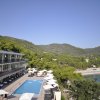 Piscina con ombrelloni vicino a un hotel e colline boscose.
