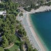Spiaggia con ombrelloni e piscina in un'area verde e rocciosa.