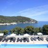Piscina con lettini e ombrelloni, vista sul mare e colline verdi.