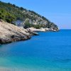 Scogliera rocciosa su mare blu, una persona nuota.