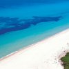Una spiaggia di sabbia bianca con acqua turchese e cespugli verdi.