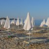 Spiaggia sabbiosa con file di lettini e ombrelloni chiusi, vicino al mare.