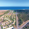 Vista aerea di un villaggio con case e vegetazione vicino al mare, diviso da una strada.