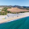 Spiaggia con ombrelloni bianchi e canoe gialle sulla sabbia, con mare blu e colline sullo sfondo.