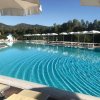 Piscina all'aperto circondata da ombrelloni bianchi e lettini, con sfondo di alberi e montagne.