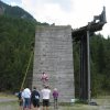 Bambina arrampica su parete di legno all'aperto, persone osservano.
