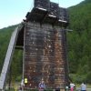 Parete d'arrampicata in legno con persone alla base, circondata da alberi.
