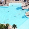 Piscina con persone che nuotano, circondata da pavimentazione e piante.