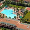Vista aerea di una piscina con ombrelloni, campi sportivi e edifici attorno.