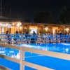 Piscina illuminata di notte con ristorante affollato sullo sfondo.