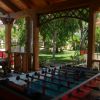 Tavolo da calcetto sotto un gazebo in legno circondato da un giardino verde.