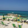 Spiaggia con sedie a sdraio e ombrelloni verdi, rivolti verso un mare azzurro brillante.