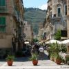Strada con edifici storici e persone che passeggiano, colline sullo sfondo.
