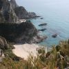 Spiaggia nascosta tra scogli con mare turchese e vegetazione.