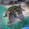 Vista aerea di una spiaggia con scogliera e mare turchese.