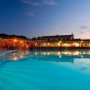 Piscina illuminata di sera con ombrelloni e sedie a sdraio.