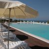 Piscina con ombrelloni e lettini bianchi vicino al mare.