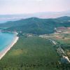 Vista aerea di una costa con spiaggia, foresta e colline sullo sfondo.