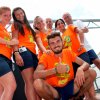 Gruppo di persone sorridenti con magliette arancioni, all'aperto.