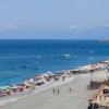 Una lunga spiaggia sabbiosa con ombrelloni colorati, una strada e auto parcheggiate.