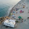 Spiaggia affollata con camper e ombrelloni.
