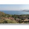 Ampio panorama costiero con colline verdi e villaggio. Mare e montagne sullo sfondo.