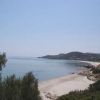 Una spiaggia sabbiosa con acqua calma, contornata da vegetazione e colline in lontananza.