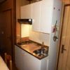 Cucina compatta con lavello, fornelli e pensili bianchi in una stanza con pareti di legno.
