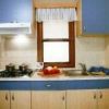 Cucina con mobili blu, lavello, fornelli e finestrella sopra il piano di lavoro.