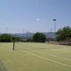 Campo da tennis all'aperto, con rete e recinzione, circondato da colline.