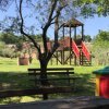Parco giochi con panchine sotto gli alberi.