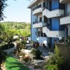 Facciata di un edificio con balconi blu, circondato da un giardino verde.