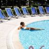 Piscina circondata da sdraio blu, persona in costume bianco si rilassa sul bordo.