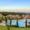 Vista panoramica di un complesso con piscina, cipressi e villette su colline verdi al tramonto.
