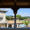 Vista di edifici in pietra con veranda, prati verdi e piscina. Alberi e colline sullo sfondo.