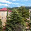 Edificio con tetto rosso attorniato da alberi alti, su sfondo collinare.