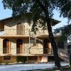 Casa di pietra con balconi, scale esterne e tre porte ad arco. Ci sono alberi davanti alla casa.