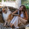 Donna seduta su una panchina in pietra con un cane peloso, sorridente.