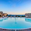 Piscina rotonda con ombrelloni e sedie, vista su colline al tramonto.